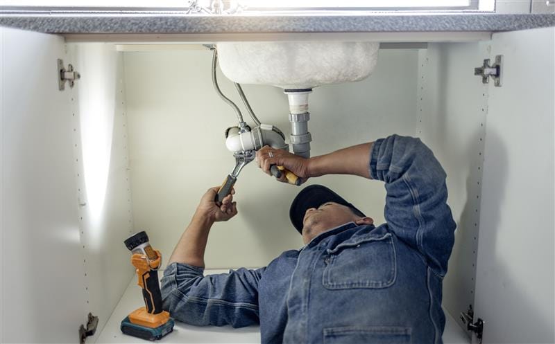 Plumber repairing pipes beneath a bathroom sink in Granite Bay